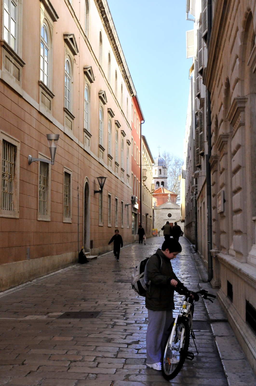 A cyclist with a bicycle in a historic street in Zadar